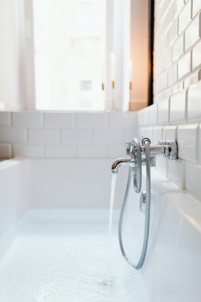 A modern white bathtub with chrome faucet and running water in a stylish tiled bathroom.