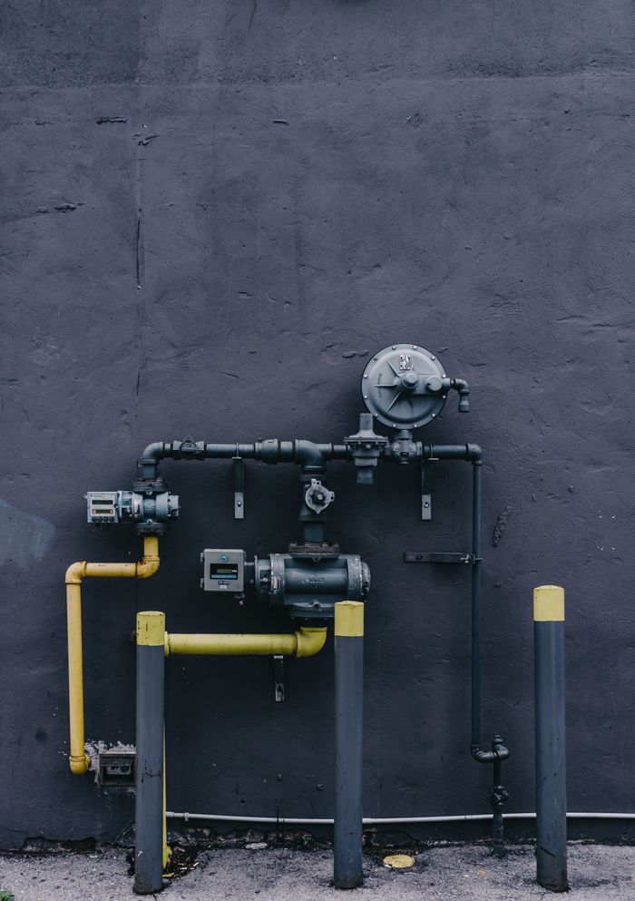 Pipes and machinery against an urban building wall with a gritty industrial look.