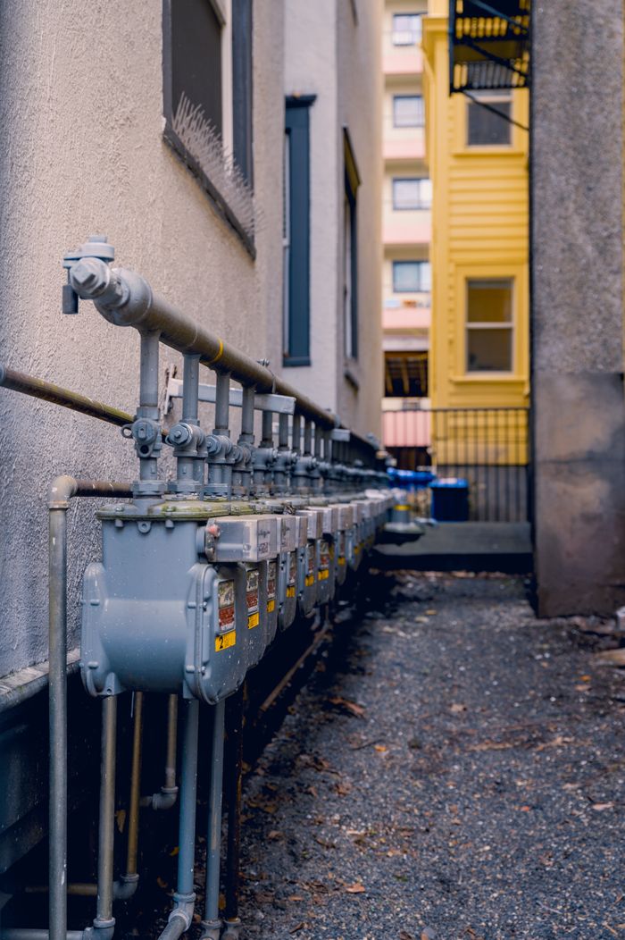 Row of gas meters with pipes in a narrow urban alleyway, captured in a vertical shot.
